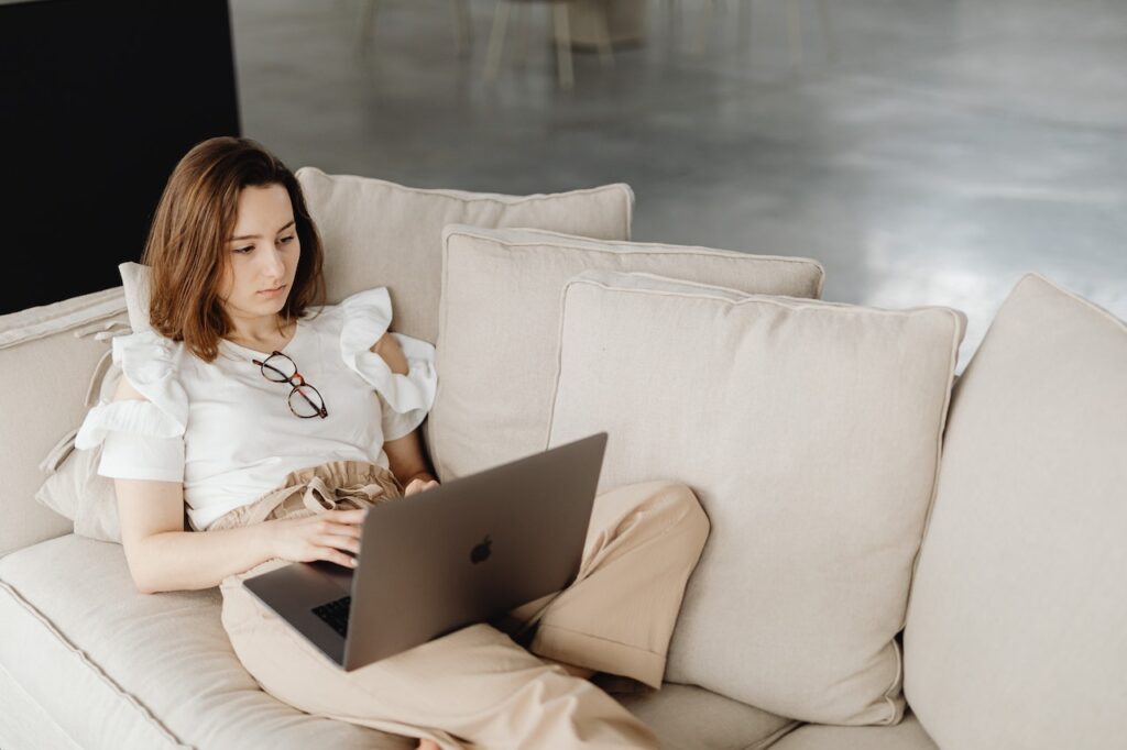 kobieta z laptopem na łóżku - stylizacja z białą koszulą i beżowymi spodniami